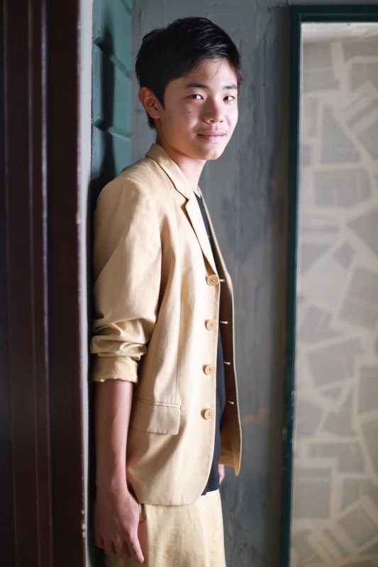 Portrait of YUUKI in a light suit, leaning against a doorway and smiling